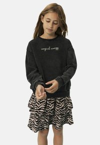 Sweat-shirt noir avec le texte "énergie magique" ; jupe rose superposée avec des rayures zébrées noires, présentée avec des manches longues et une coupe décontractée.