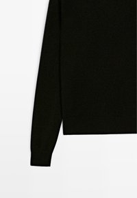 Pull en maille noire à manches longues, raccourci du côté droit, montrant une manche et un ourlet côtelé sur fond blanc uni.