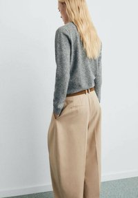 Pull en tricot gris à manches longues associé à un pantalon large beige avec poches latérales et une ceinture marron. Design minimaliste.