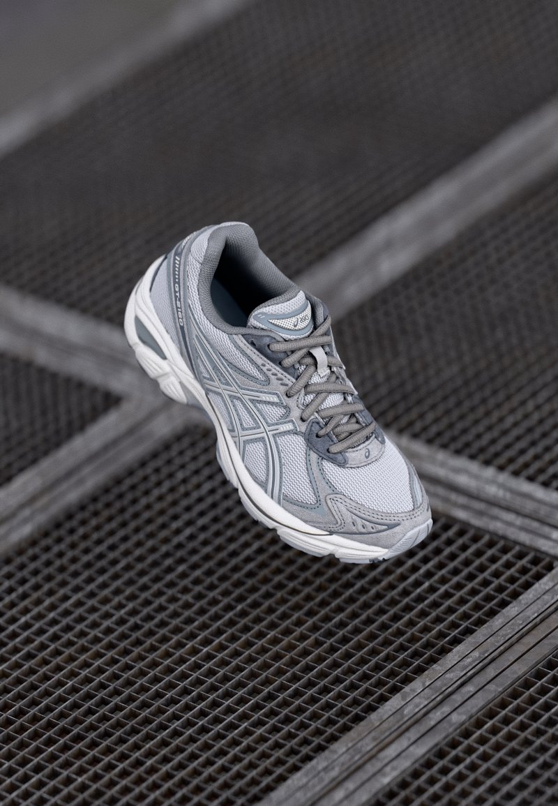 Chaussure de sport grise avec tige en mesh, semelle en caoutchouc et col rembourré. Comprend des lacets, un design texturé et des accents réfléchissants.