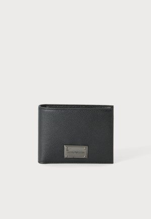 Portefeuille noir en cuir bi-pli avec une plaque logo métallique rectangulaire sur le devant, présenté sur un fond clair uni.