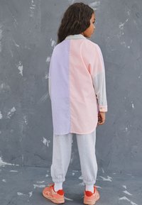 Long-sleeve shirt in pink and lavender stripes, paired with grey joggers. The shirt has a curved hem and button detailing on the sleeves.