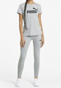 Grå idrottsset som inkluderar en t-shirt och leggings, båda med den svarta "PUMA"-logotypen. T-shirten har rundad halsringning, och leggingsen är figurnära.