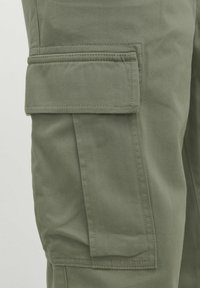 Olive green cargo pants feature a side pocket with flap, sturdy fabric, relaxed fit, and reinforced stitching along the seams.