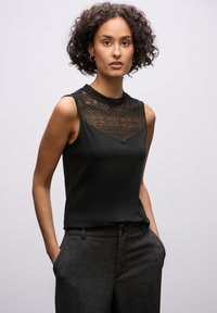 Top senza maniche nero con dettagli in pizzo sul colletto, abbinato a pantaloni grigi scuri. Tessuto liscio con un motivo in pizzo strutturato.