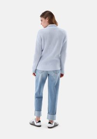 Hellblauer gerippter Pullover mit Kragen, kombiniert mit hellblauen Hochwasserjeans und schwarz-weißen Turnschuhen.