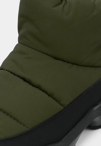 Párnázott zöld csizma fekete alappal, tűzött textúrával és lekerekített formával, a melegség és kényelem érdekében tervezve.