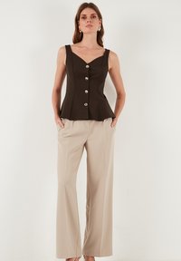Brah peplum top s srebrnimi gumbi, v kombinaciji z lahkimi bež širokimi hlačami. Gladka tekstura, prilegajoča zasnova in brezrokavni stil.
