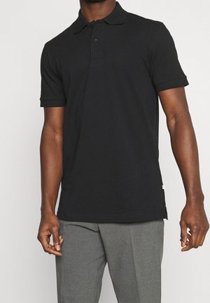 Schwarzes Poloshirt mit klassischem Kragen, Drei-Knopf-Leiste, kurzen Ärmeln und glatter Baumwollstruktur. Kombiniert mit grauen Hosen.