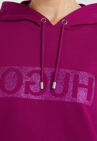 Sweat à capuche fuchsia avec logo pailleté métallique, cordons avec embouts en métal argenté, tissu doux et coupe décontractée.