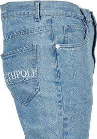 Los pantalones de mezclilla de un azul claro presentan un diseño de pierna recta, con un bolsillo trasero que muestra el logo "SOUTHPOL" y un detalle de botón plateado.