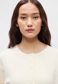 Ανοιχτό μπεζ πλεκτό πουλόβερ με στρογγυλή λαιμόκοψη και κουμπί με πέντε κουμπιά, λεία υφή και χωρίς ορατά σχέδια.