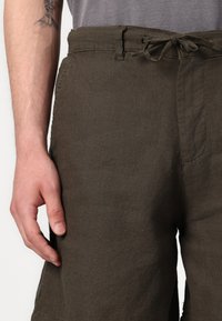 Shorts en lin vert foncé avec une coupe décontractée, dotés d'une taille à cordon de serrage et de poches latérales, affichant un tissu texturé.