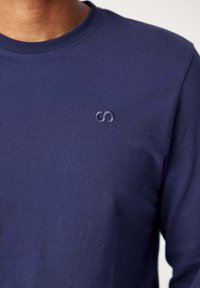 Maglietta a maniche lunghe color blu navy realizzata in cotone morbido con scollo a costine e logo ricamato sottile sul petto. Texture liscia, forma aderente.