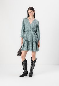 Teal blomsterkjole med v-hals, lagdelte nivåer og lange puff sleeves. Kombinert med svarte broderte cowboystøvler og en liten veske.