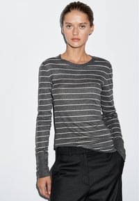 Szara koszula z długim rękawem w białe poziome paski, z okrągłym dekoltem i miękką teksturą, zestawiona z czarnymi spodniami.