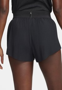 Mustat laskostetut shortsit, joissa on teksturoitu vyötärönauha ja siksakreuna. Etuosassa on verkkokangasosa ja takana pieni logotunniste.