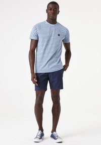 Camiseta azul de rayas con cuello redondo, combinada con pantalones cortos de color marino. La camiseta tiene un pequeño parche con un logo y se complementa con zapatillas azules.