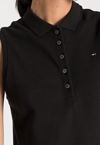 Polo shirt senza maniche nera realizzata in tessuto testurizzato, con colletto e sei bottoni neri, arricchita da un piccolo logo.