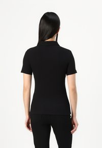 Svart kortärmad polo t-shirt med krage, figursydd design och slät textur, kombinerad med svarta byxor. Visar upp en elegant, minimalistisk stil.