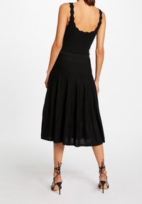 Schwarzes Kleid mit gewellten Trägern, gerippter Textur, figurbetontem Oberteil und fließendem, knielangem Rock. Getragen mit schwarzen, schlichten High Heels.
