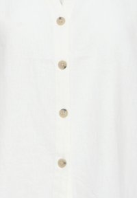 Tissu blanc avec une rangée verticale de quatre boutons beige brillants cousus au centre.