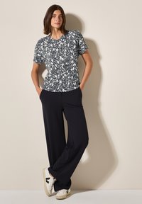 Patroon korteblauwe V-hals top in zwart en wit, gecombineerd met losse zwarte broeken en witte sneakers met zwarte accenten.