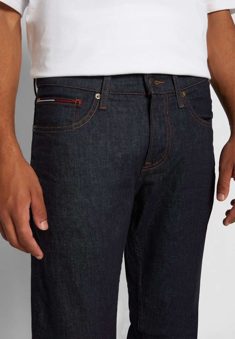 Donker denim jeans gemaakt van katoen met oranje stiksels. Bevat een voorzak met een meerkleurig ontwerp en een knoopsluiting in de taille.