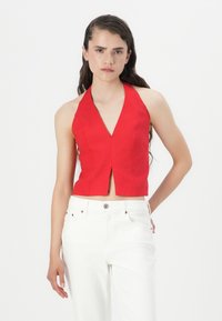Top court rouge à col halter avec un décolleté en V profond et une fente à l'avant, en tissu texturé. Assorti à un jean blanc taille haute.
