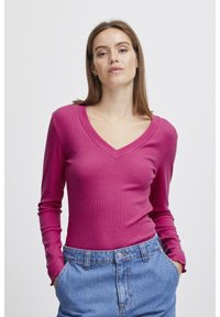 Fitted långärmad topp i livfull rosa ribbad tyg med V-ringning, kombinerad med högmidjade denimshorts med knappstängning.
