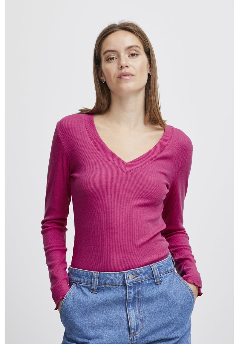 Fitted långärmad topp i livfull rosa ribbad tyg med V-ringning, kombinerad med högmidjade denimshorts med knappstängning.