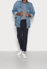 Kurtka dżinsowa w jasnym odcieniu, zestawiona z granatową koszulą w paski, ciemnymi spodniami i białymi sneakersami. Charakteryzuje się luźnym krojem i casualowym stylem.