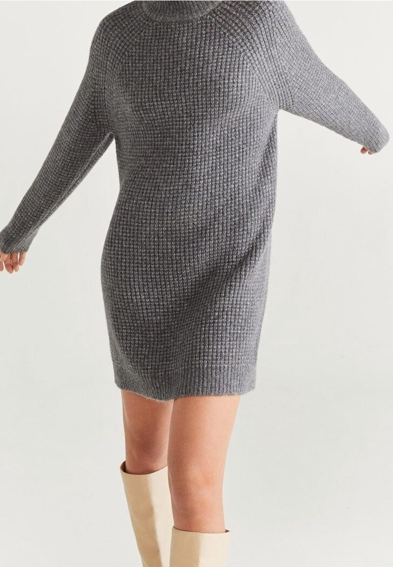 Šedé pletené šaty s vysokým límcem, dlouhými rukávy a texturovaným vzorem, sahající po střední stehno, doplněné krémovými botami po kolena.