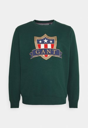 Ciemnozielona bluza z dużym, haftowanym herbem w kształcie tarczy z gwiazdami, paskami i napisem „GANT” na środku przodu.