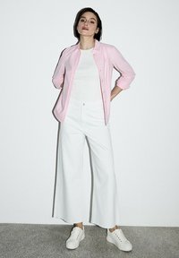 Jasnoróżowa koszula zapinana na guziki, biały podkoszulek, szerokie białe spodnie i białe trampki. Gładki materiał i luźny krój z podwiniętymi rękawami.