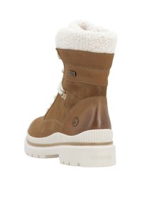 Botín de ante marrón con un cuello de pelo sintético blanco, diseño de cordones, suela de goma y logo grabado en el lateral. Punta y talón reforzados.