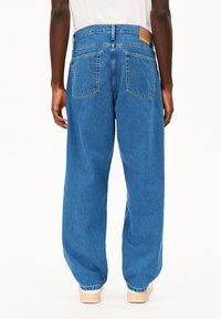 Baggy blauwe denim jeans met een hoge taille, grote achterzakken en een leren patch in bruin op de tailleband. Gladde textuur en klassiek ontwerp.