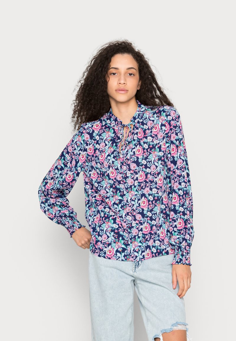 Blusa de manga longa em azul-marinho com padrão floral, apresentando flores rosas e azuis, decote franzido e punhos elásticos. Feita de um tecido suave.