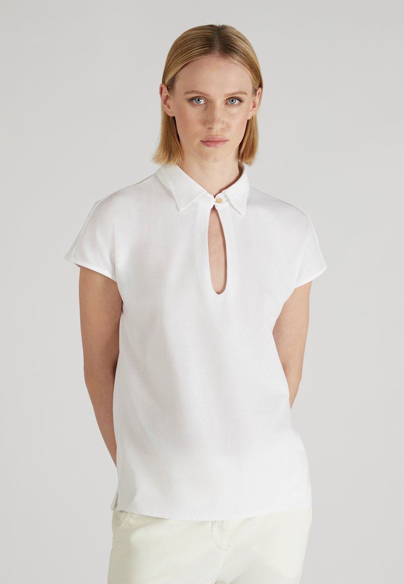 Blusa bianca a maniche corte con colletto e apertura a chiave sul davanti, caratterizzata da una leggera lucentezza e linee pulite.