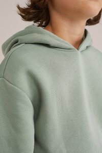 Felpa verde menta con una texture morbida, dotata di cappuccio e dettagli a coste sul colletto e sui polsini. La vista ravvicinata mette in risalto i dettagli del tessuto.