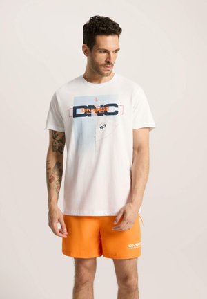 Biała bawełniana koszulka z grafiką w niebiesko-pomarańczowym kolorze z napisem "DIVERSE" i kotwicą. Połączona z jasnopomarańczowymi szortami.