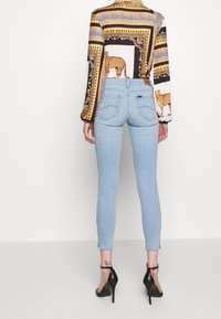 Ljusblå skinny jeans med hög midja, med en slät denimstruktur och bakfickor; kombinerat med en mönstrad långärmad blus.