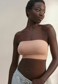 Nude naadloze bandeau beha met een textuur elastische band met reliëfbranding, gedragen met grijze sweatpants met trekkoord. Glad stofafwerking.