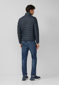 Granatowa, pikowana kurtka z wysokim kołnierzem i poziomymi przeszyciami, zestawiona z niebieskimi dżinsami i ciemnymi trampkami.