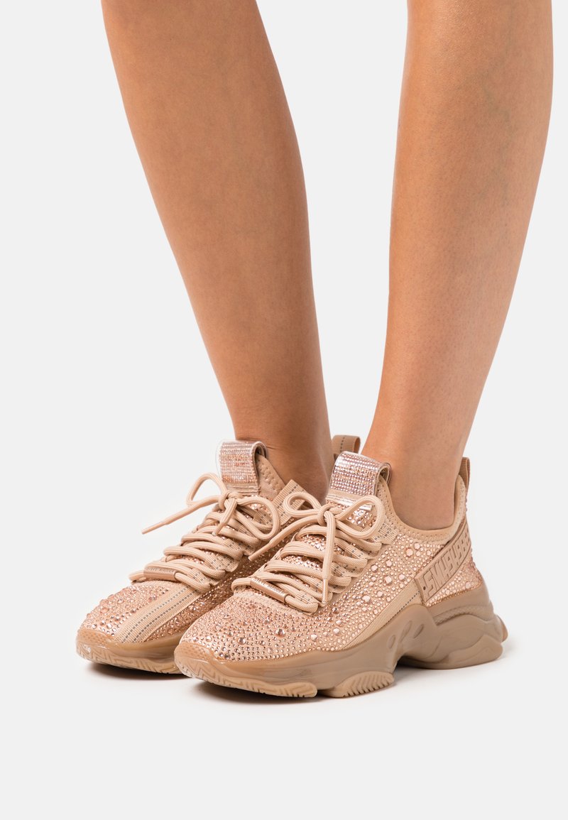 Sneakers atletiche beige con tomaia texturizzata, impreziositi da strass, dotati di lacci e un'etichetta con logo sul lato.