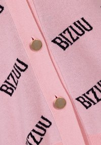 Roze gebreide cardigan met zwart "BIZUU" logo patroon, ronde gouden knopen en een zachte textuur.