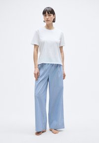 T-shirt en coton blanc à manches courtes, associé à un pantalon large à rayures bleu clair, avec des motifs verticaux bleus et blancs.