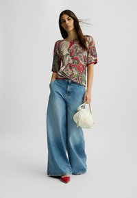 Top con stampa paisley multicolore, vestibilità comoda, maniche corte, abbinato a jeans in denim blu a gamba larga. Accessoriato con una piccola borsa bianca.