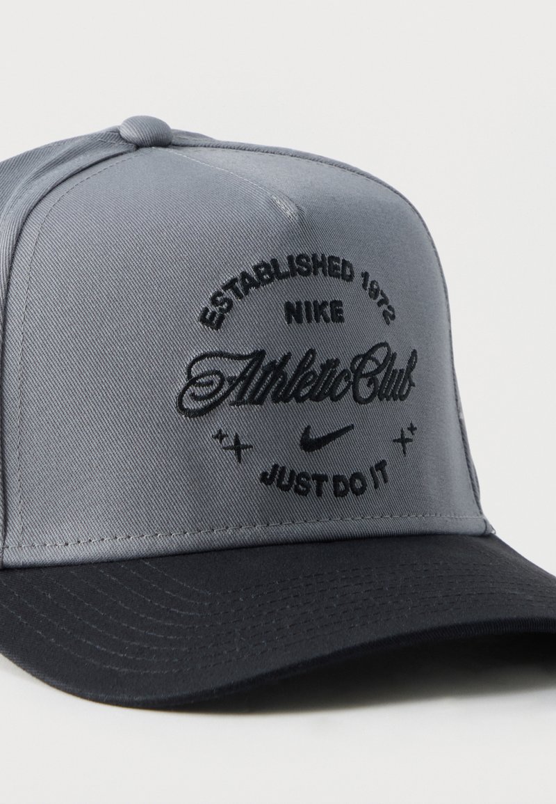 Grau-schwarze Nike-Baseballkappe mit eingesticktem Text "Established 1972 Nike Athletic Club" und dem Slogan "Just Do It" auf der Vorderseite.