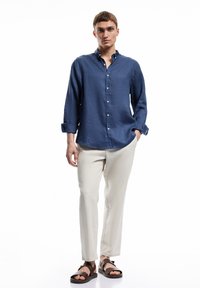 Donkerblauw linnen overhemd met lange mouwen, gecombineerd met lichtbeige broeken en bruine sandalen. Gladde textuur, klassieke stijl.